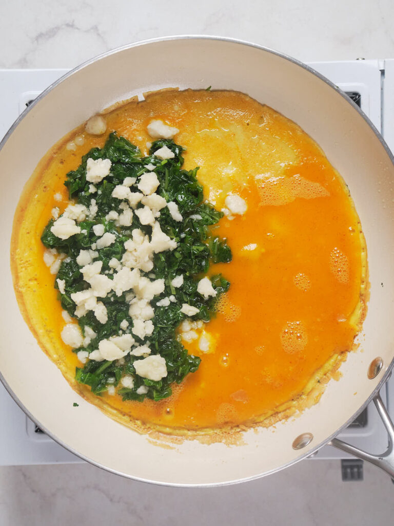 Cheese and spinach omelet being cooked in a pan.