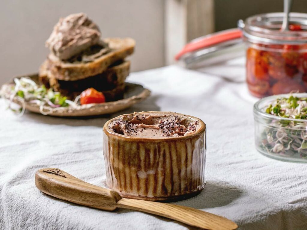 A ceramic container filled with spread sits on a table with a wooden spatula.