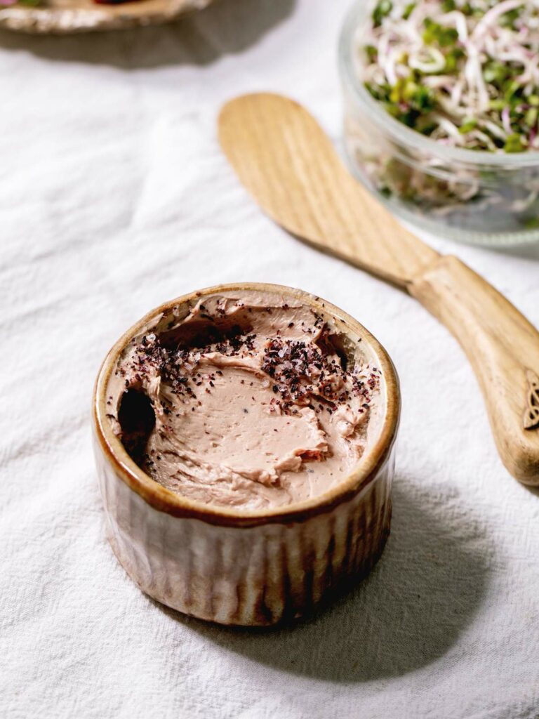 A small ceramic dish filled with a creamy spread, topped with a sprinkle of herbs.
