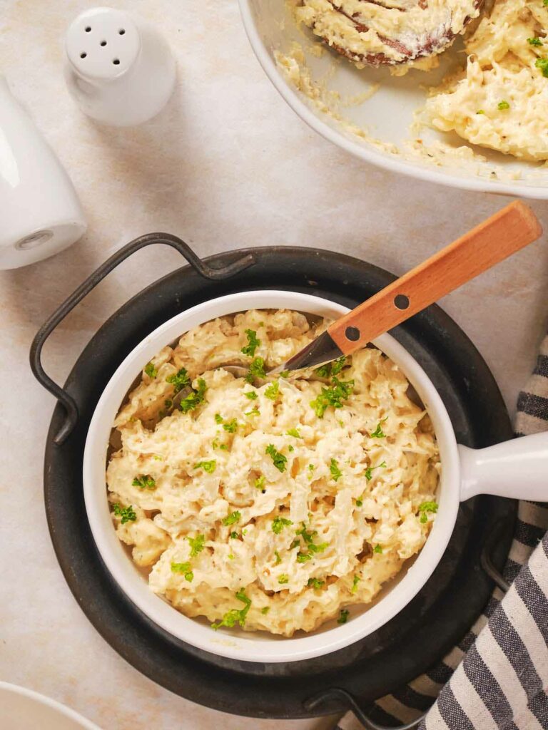 A bowl of mashed potatoes with herbs on top, accompanied by a knife with a wooden handle.