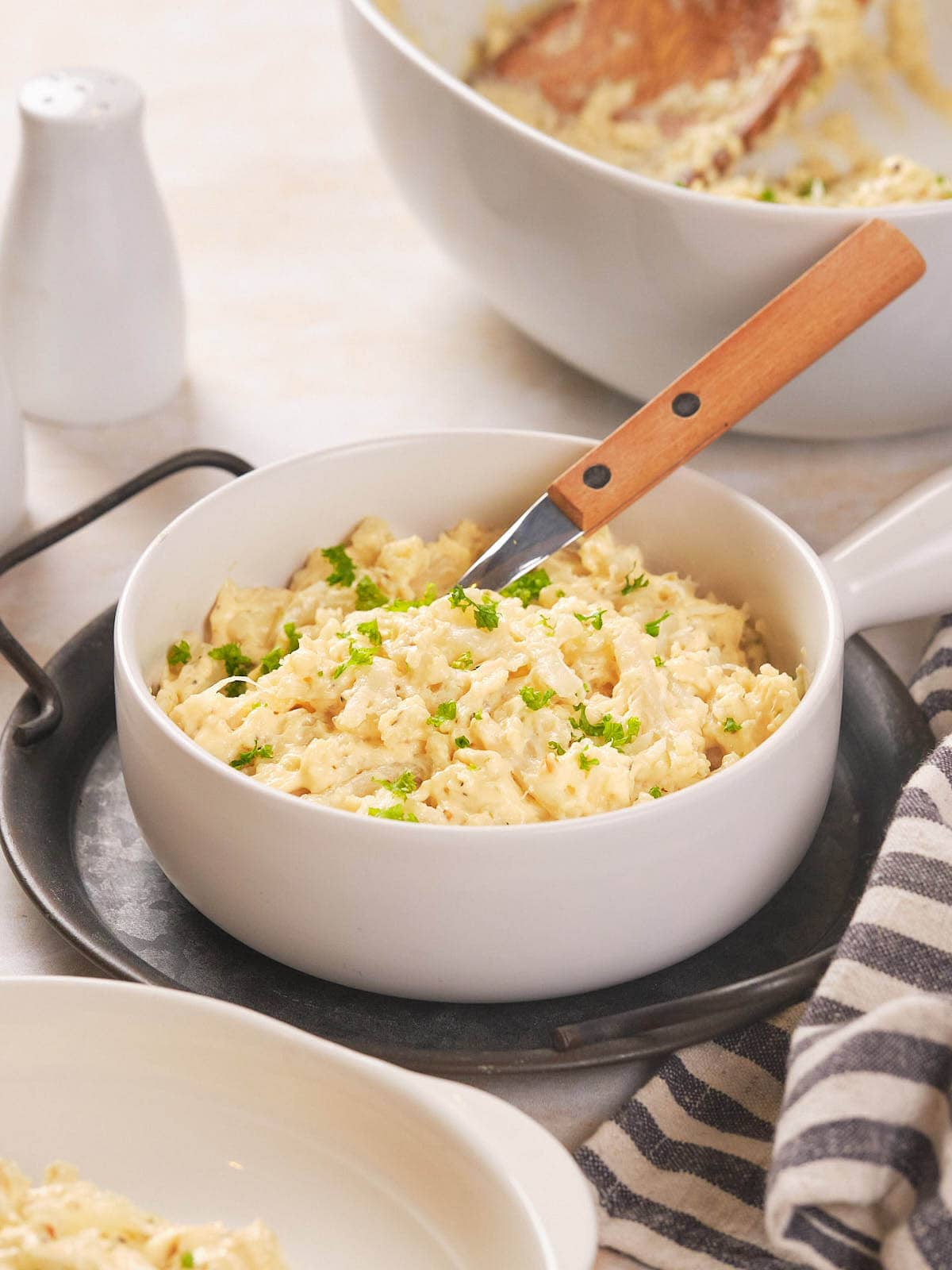 A white bowl filled with scrambled cauliflower garnished with chopped herbs.