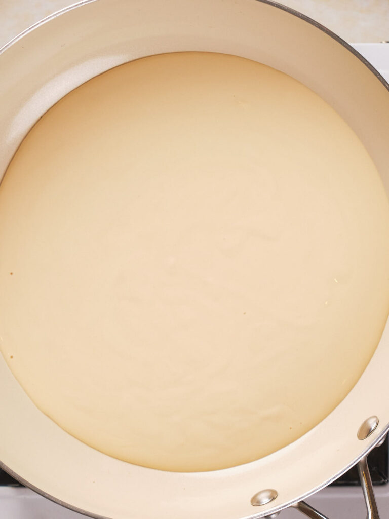A close-up view of a creamy liquid in a white frying pan.