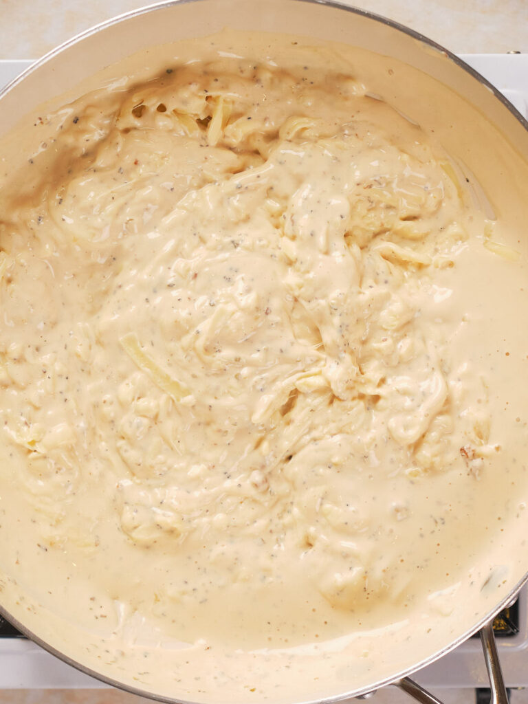 A close-up of a pan filled with creamy, light beige sauce, with visible herbs and spices.