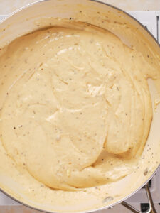 A close-up of creamy sauce with visible herbs cooked in a large pan.