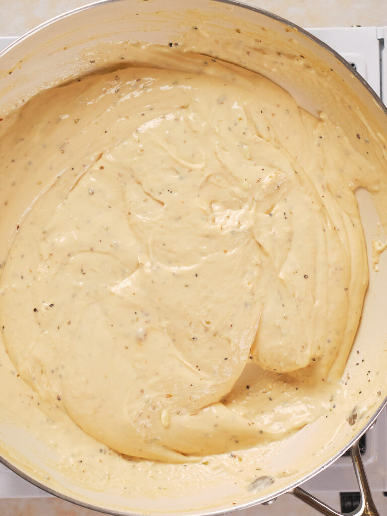 A close-up of creamy sauce with visible herbs cooked in a large pan.