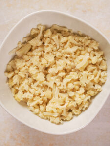 A white bowl filled with chopped cauliflower pieces on a light surface.