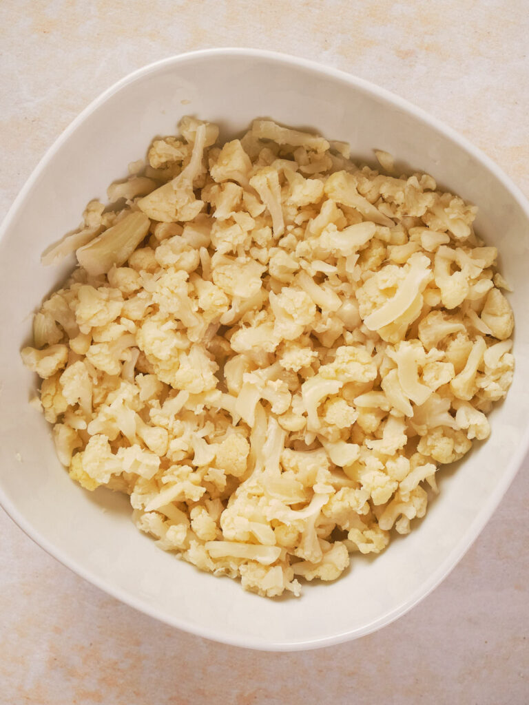 A white bowl filled with chopped cauliflower pieces on a light surface.