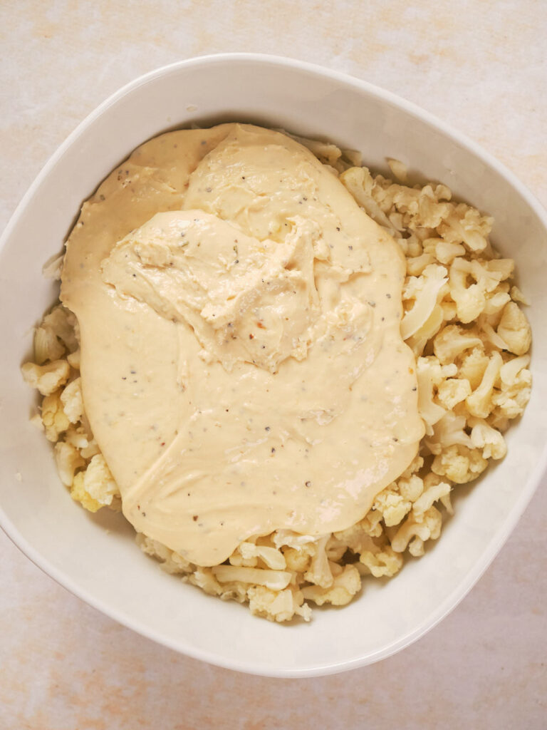 A white bowl filled with chopped cauliflower topped with a thick, creamy sauce.