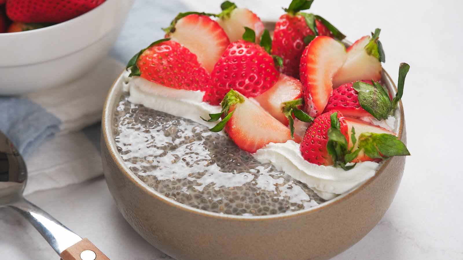 A bowl of chia pudding topped with whipped cream and fresh strawberry slices.