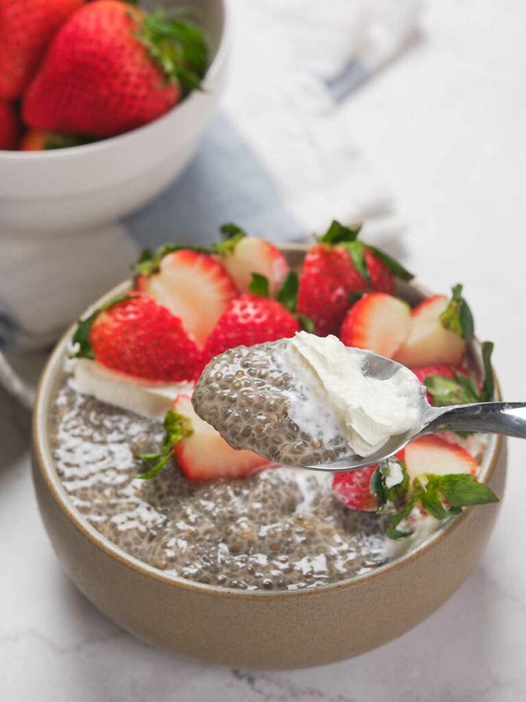A bowl of chia pudding topped with sliced strawberries, with a spoonful of pudding and cream held above it.