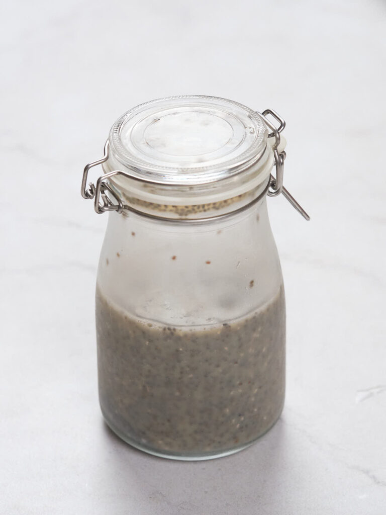 A glass jar with a clasp lid containing chia pudding is placed on a light-colored surface.