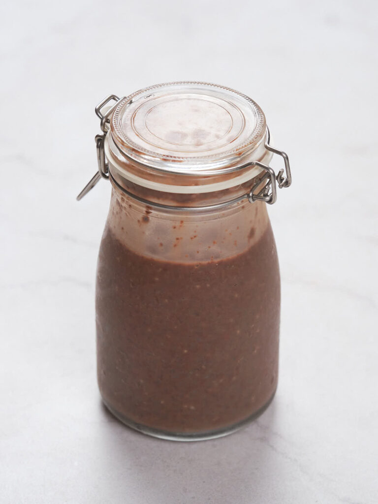 A glass jar with a hinged lid filled with chia pudding sits on a light-colored surface.