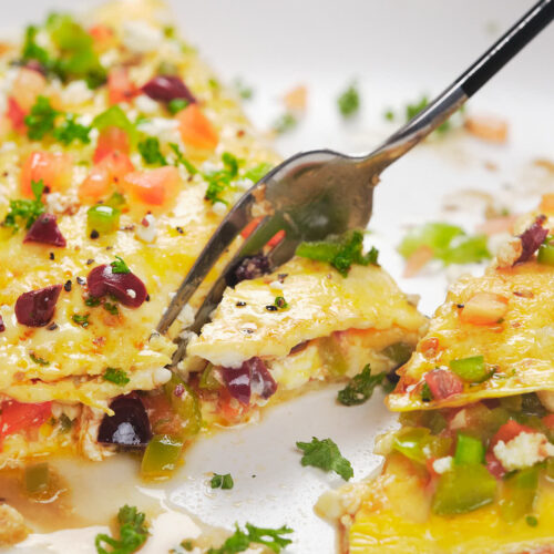 A fork cutting into a colorful vegetable omelet on a white plate.