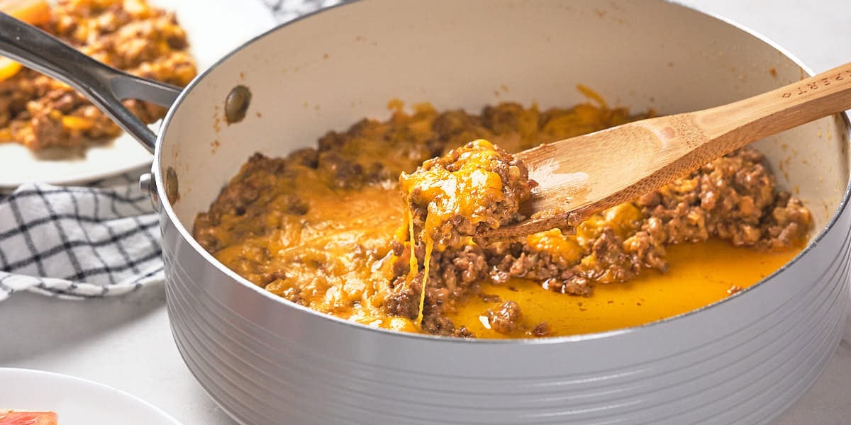 A cooking pot filled with a cheesy ground beef mixture, with a wooden spoon holding a portion.