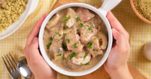 A person holds a bowl of slow cooker stroganoff with mushrooms and parsley garnish.