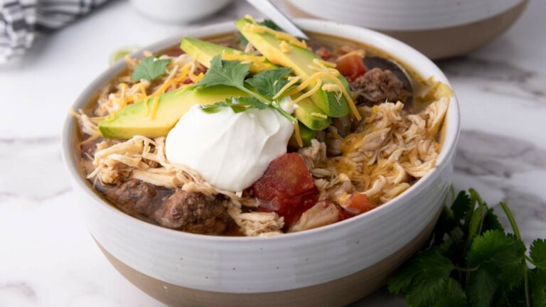 A bowl of taco soup topped with avocado slices, sour cream, shredded cheese, and cilantro.