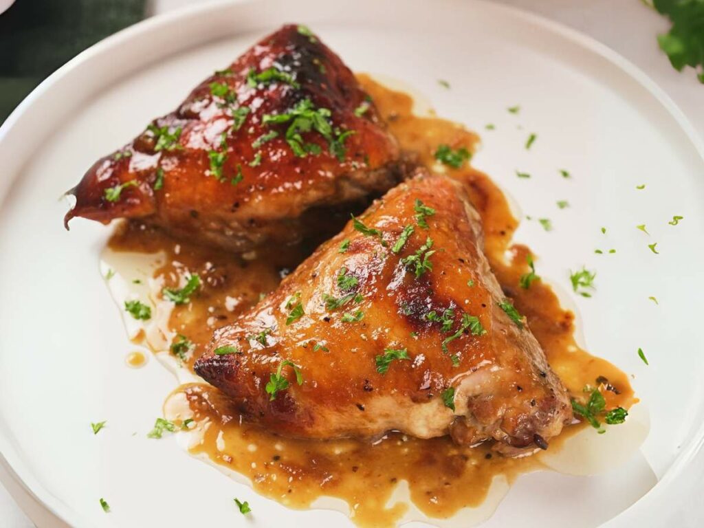 Two pieces of apricot chicken with green garnish on a white plate, drizzled with sauce.