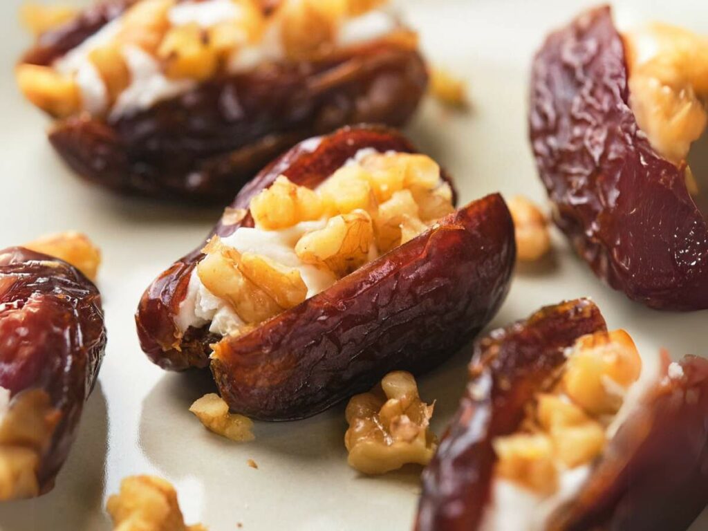 Close-up of dates stuffed with goat cheese and chopped walnuts on a light-colored plate.