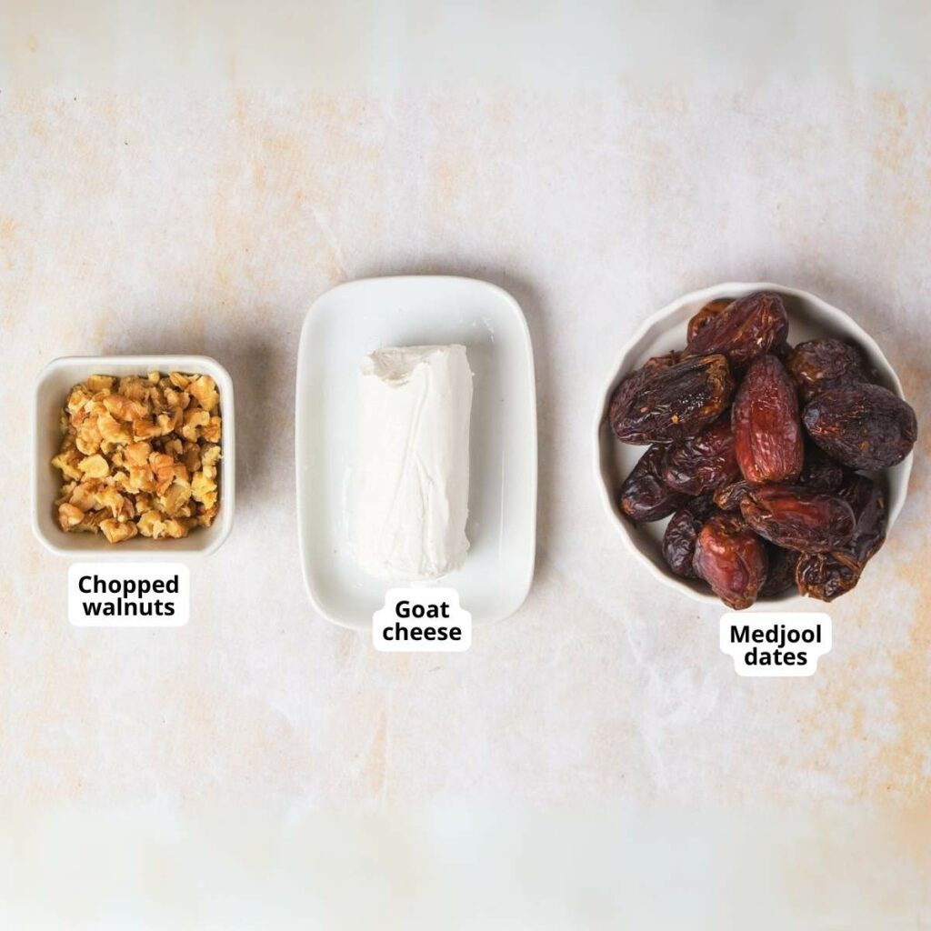 Three bowls containing chopped walnuts, a block of goat cheese, and Medjool dates, labeled respectively on a light background.
