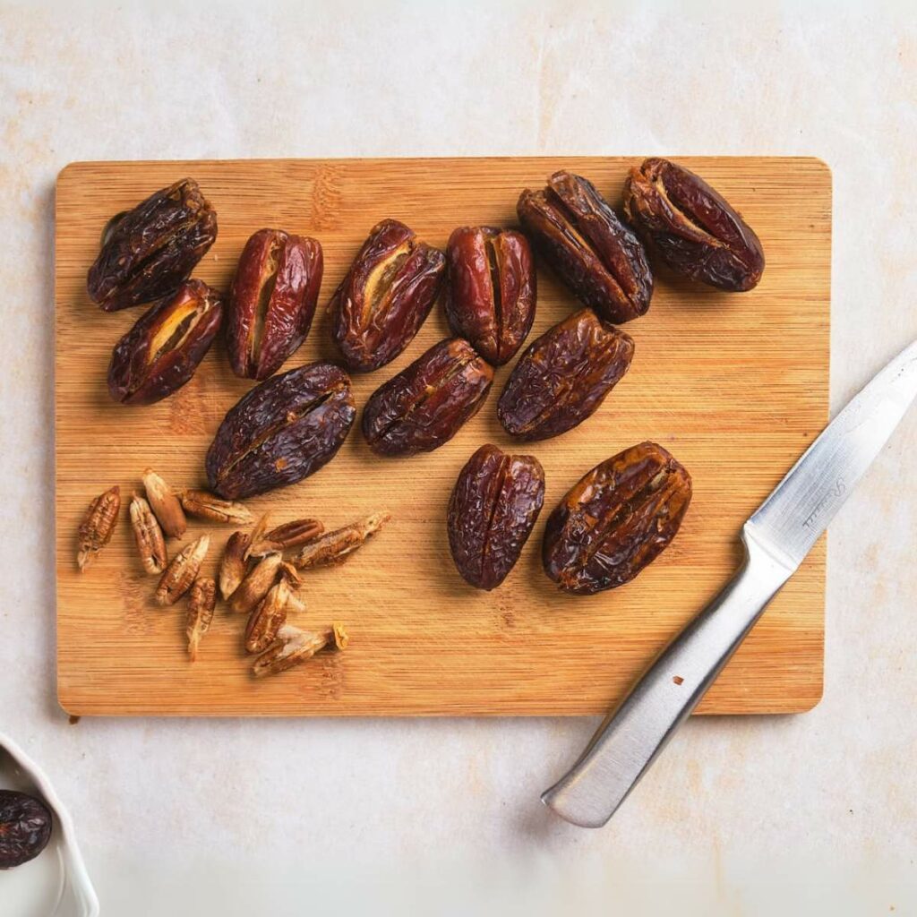 A wooden cutting board with sliced dates and removed seeds beside a knife.