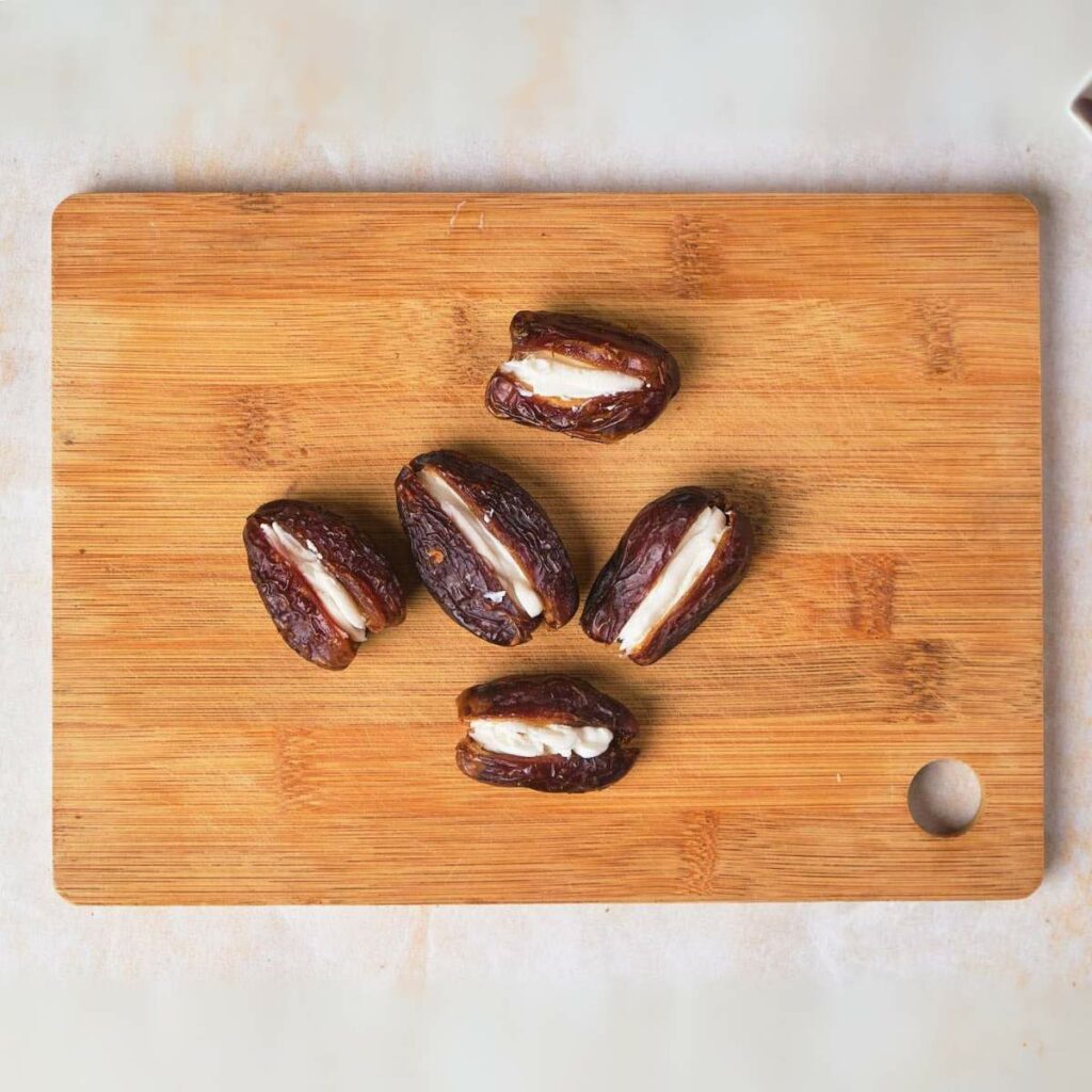 Six stuffed dates placed on a wooden cutting board.