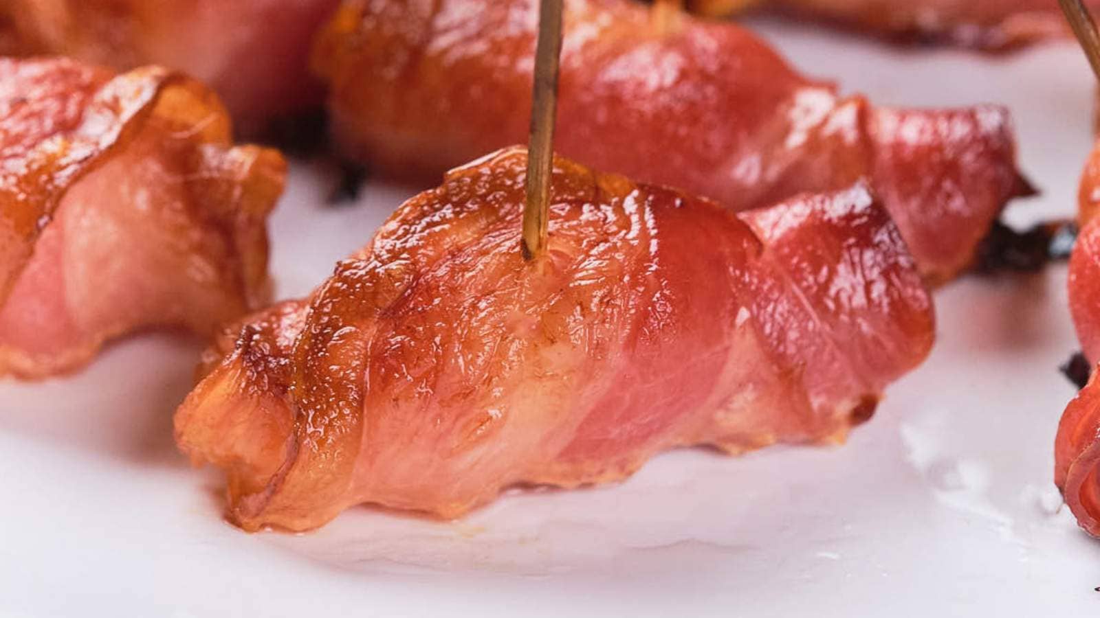Close-up of pineapple and bacon bites on a white plate, secured with toothpicks.