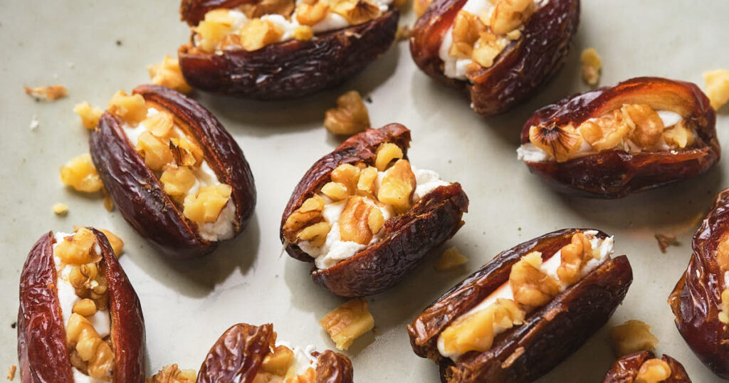 Dates stuffed with goat cheese and chopped walnuts on a light green background.