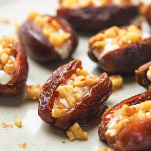Dates stuffed with chopped nuts and goat cheese arranged on a plate.
