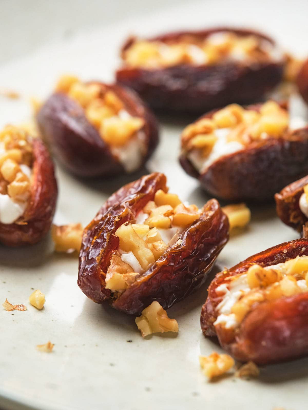 Dates stuffed with chopped nuts and goat cheese arranged on a plate.