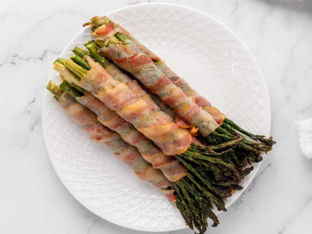 Bacon-wrapped asparagus spears arranged neatly on a white plate.
