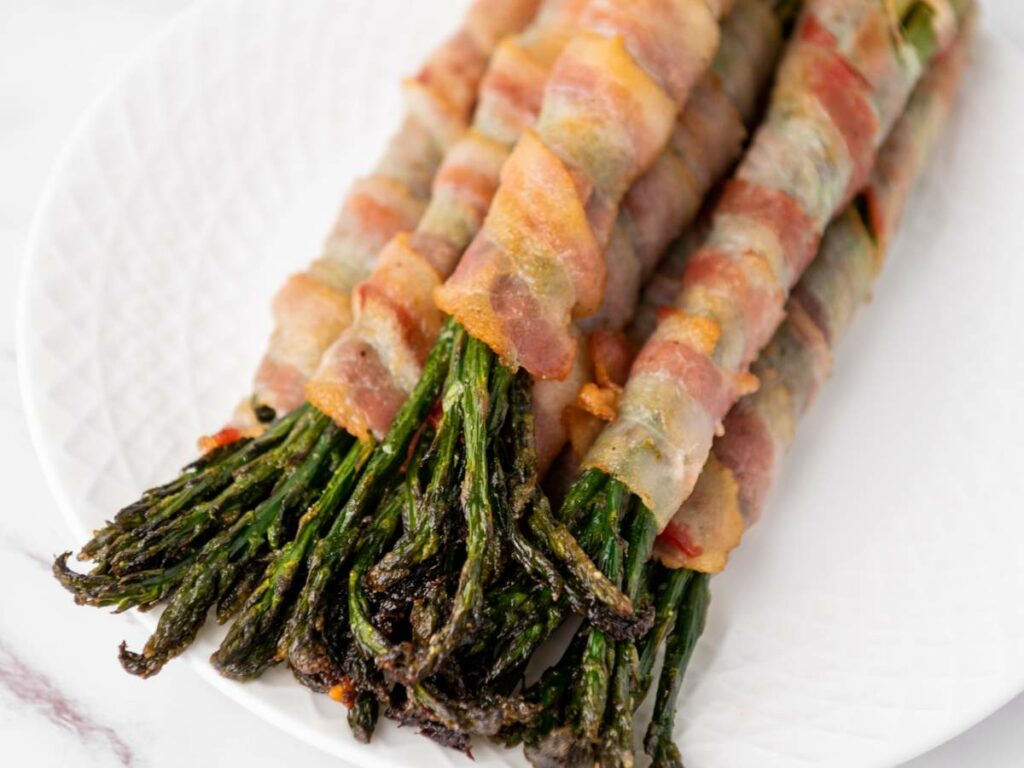 Bacon-wrapped asparagus spears arranged on a white plate.