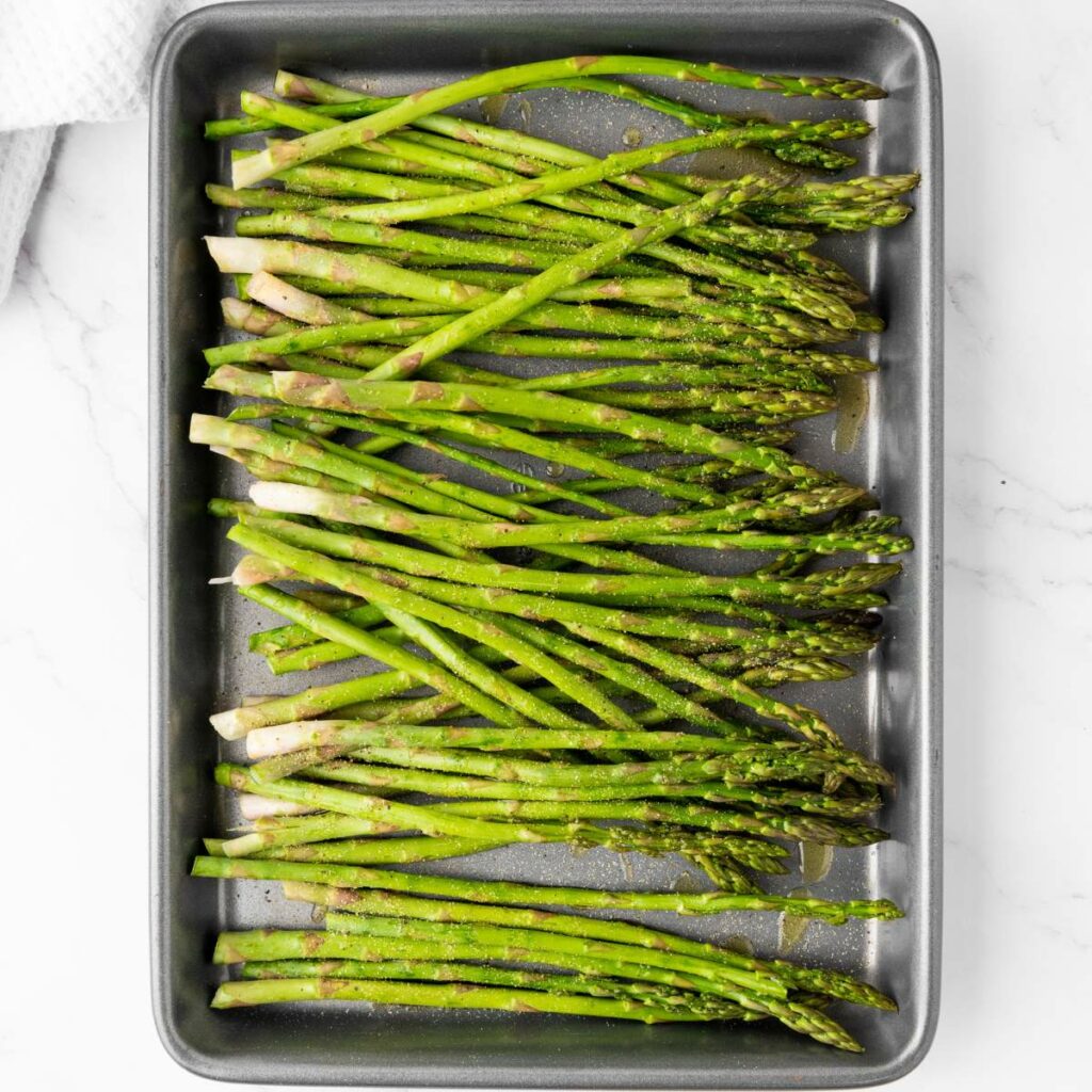 Fresh asparagus spears arranged on a baking tray, lightly seasoned with salt and pepper, ready for roasting.