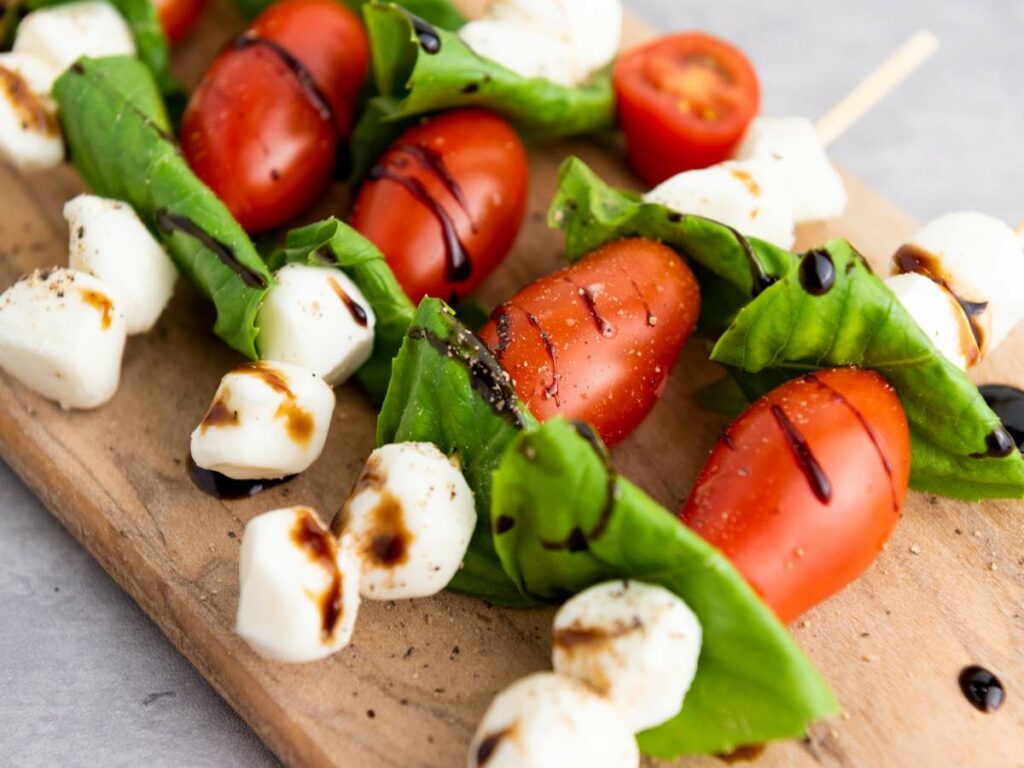 Caprese appetizer with cherry tomatoes, fresh mozzarella, and basil leaves on a wooden board, drizzled with balsamic glaze.