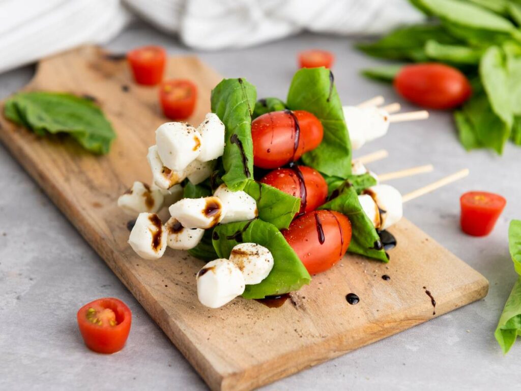 Caprese appetizer with cherry tomatoes, mozzarella, and basil on a wooden board, drizzled with balsamic glaze.
