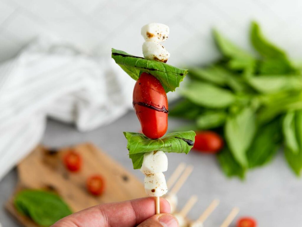 Close-up of a caprese appetizer with mozzarella balls, a cherry tomato, and basil leaves.