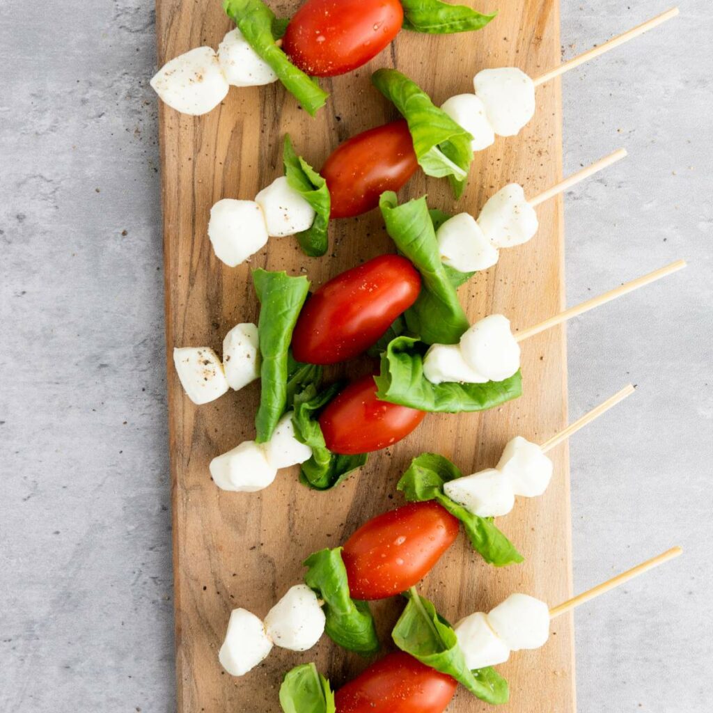 Skewers with cherry tomatoes, mozzarella, and basil leaves on a wooden board.