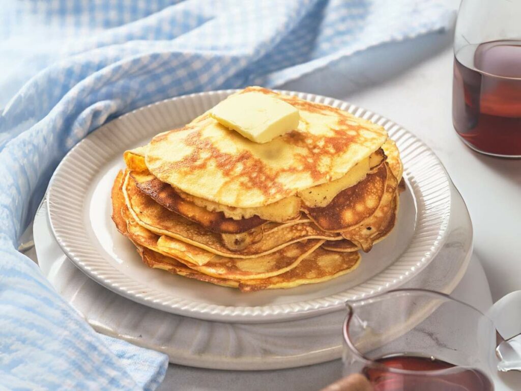 A stack of pancakes with a pat of butter on top, served on a white plate.