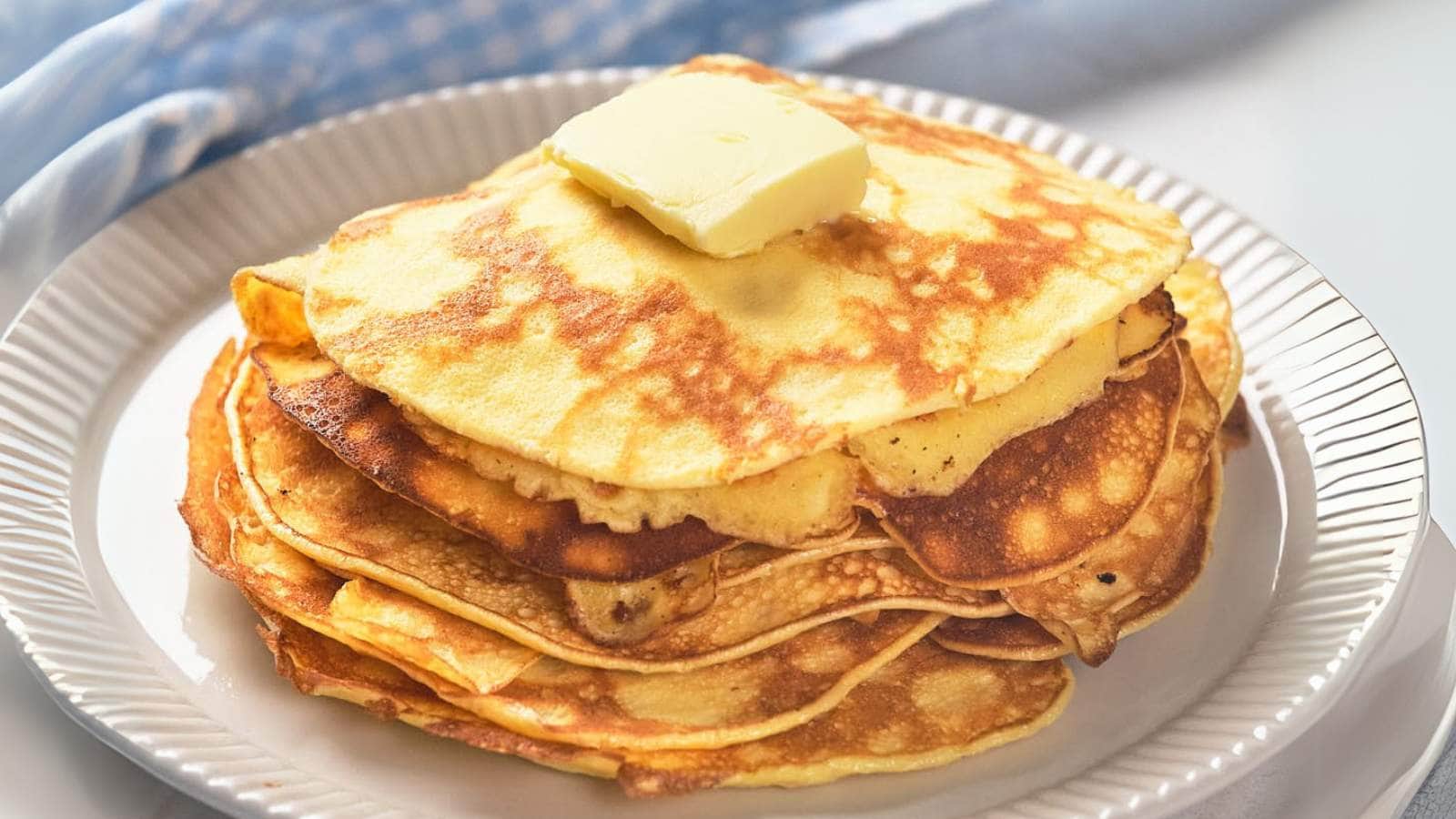 A stack of golden pancakes topped with a square of butter on a white plate.
