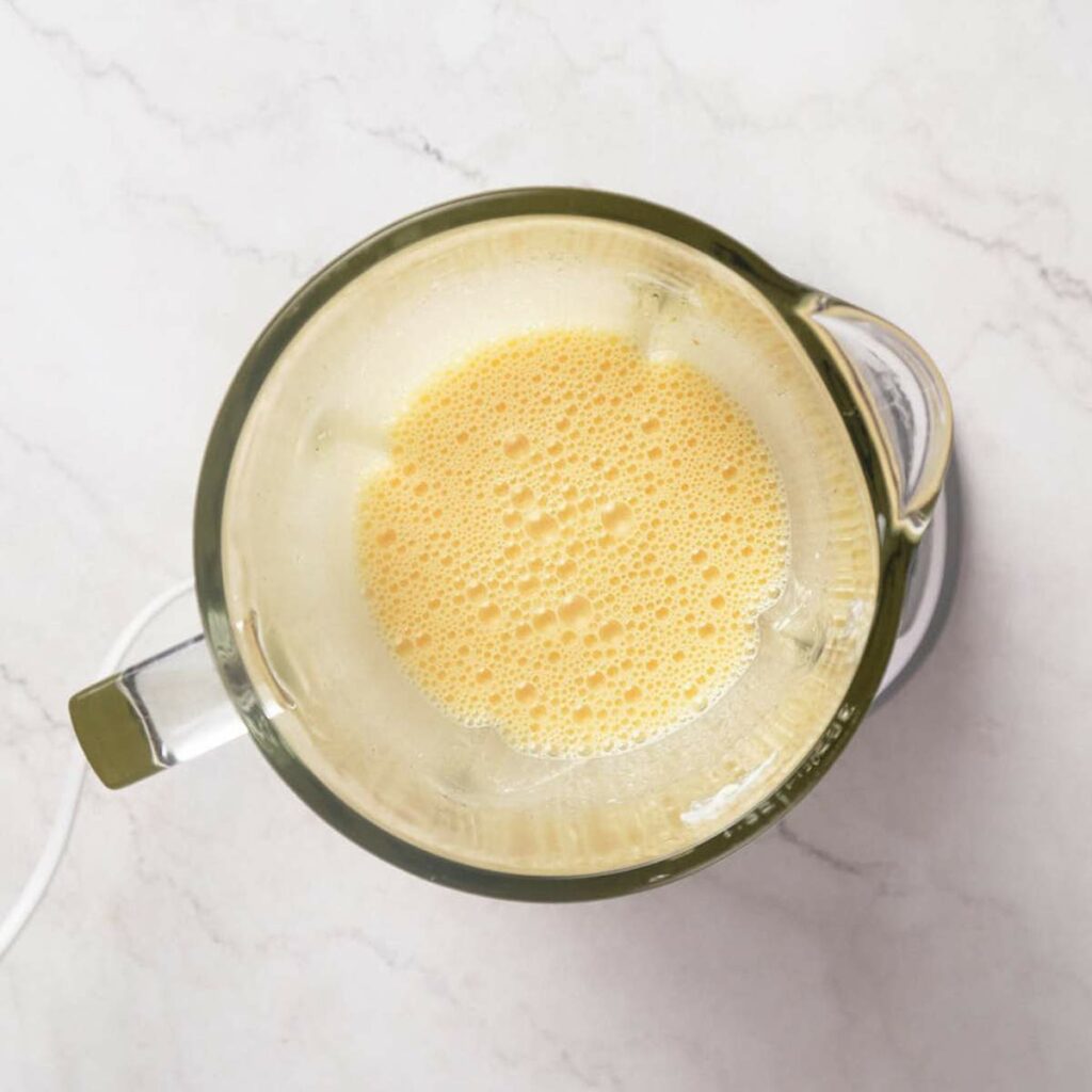 Top view of a blender containing frothy, yellow liquid on a white countertop.