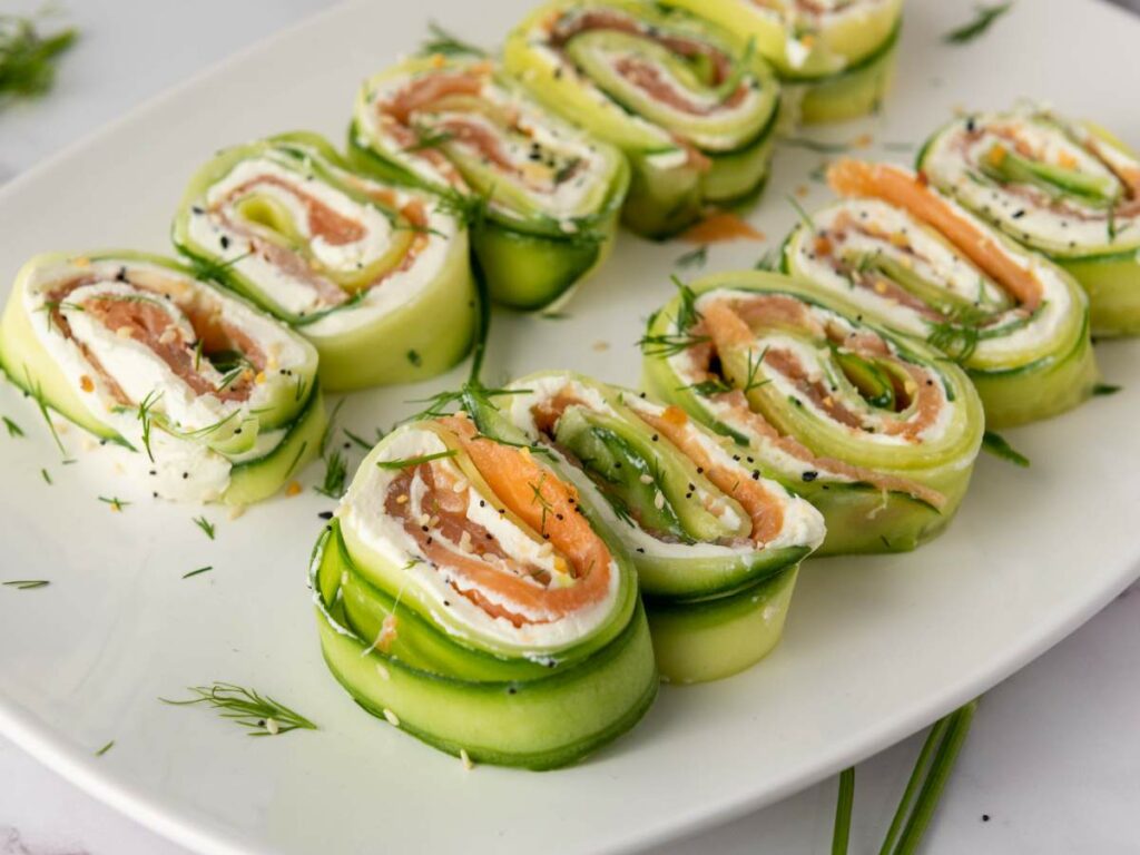 Sliced cucumber roll ups on a white plate, garnished with dill and black sesame seeds.