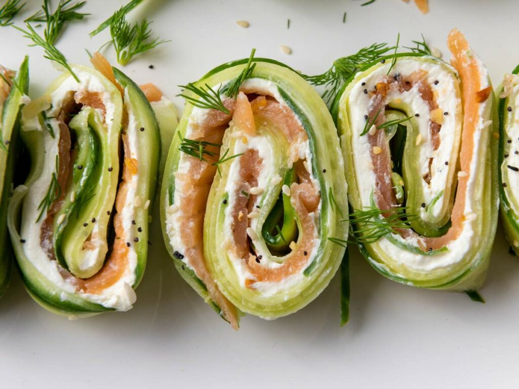 Close-up of rolled cucumber slices filled with cream cheese, smoked salmon, and herbs.