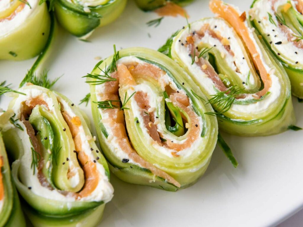 Close-up of rolled cucumber slices filled with cream cheese, smoked salmon, and garnished with fresh dill.