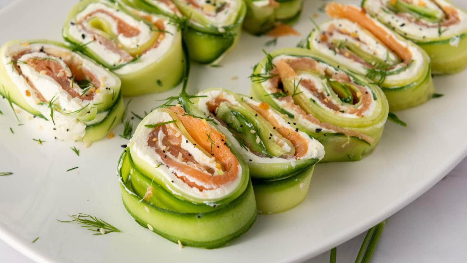 Cucumber roll ups on a plate filled with cream cheese, smoked salmon, and garnished with dill.