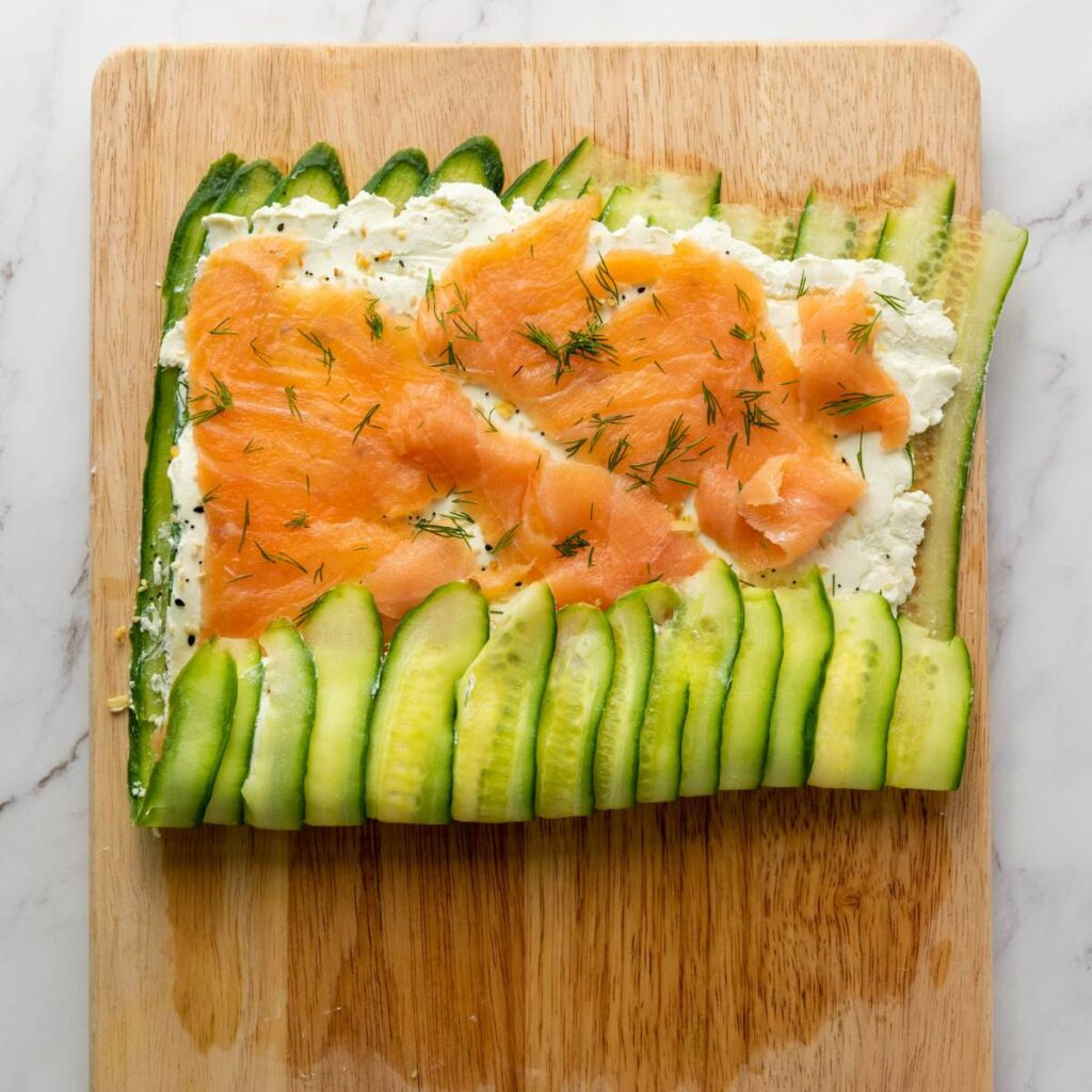Cucumber slices topped with cream cheese, smoked salmon, and dill on a wooden board.