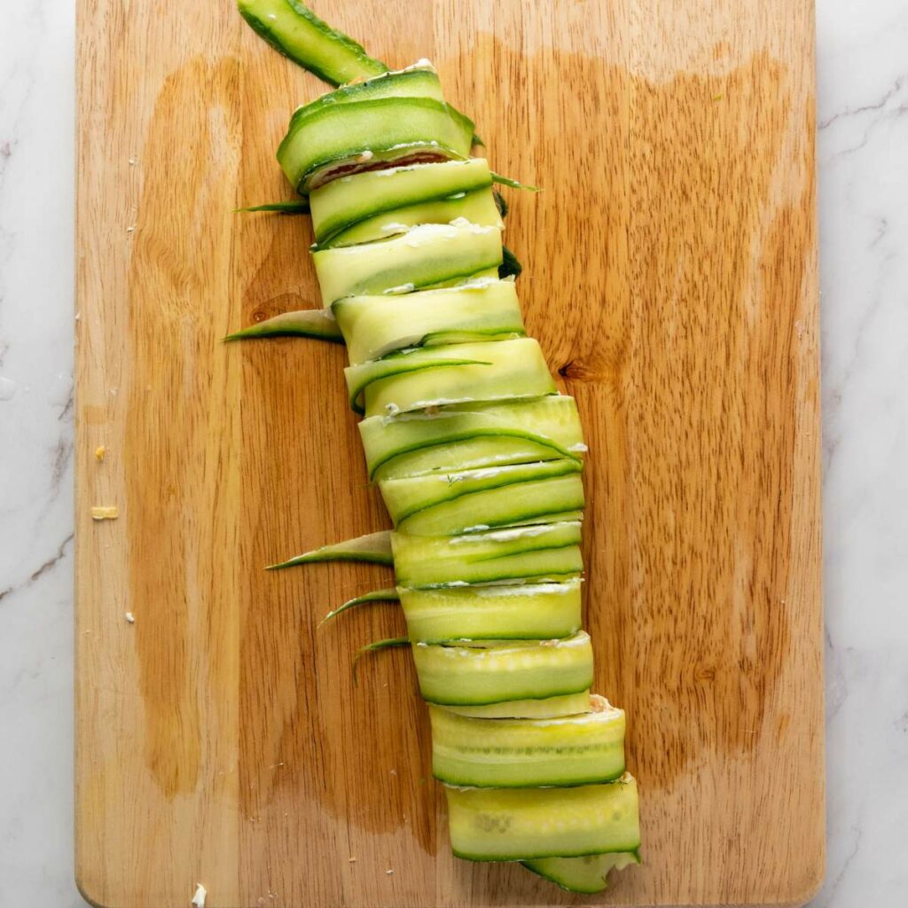 Thinly sliced zucchini wrapped around a filling, placed on a wooden cutting board.