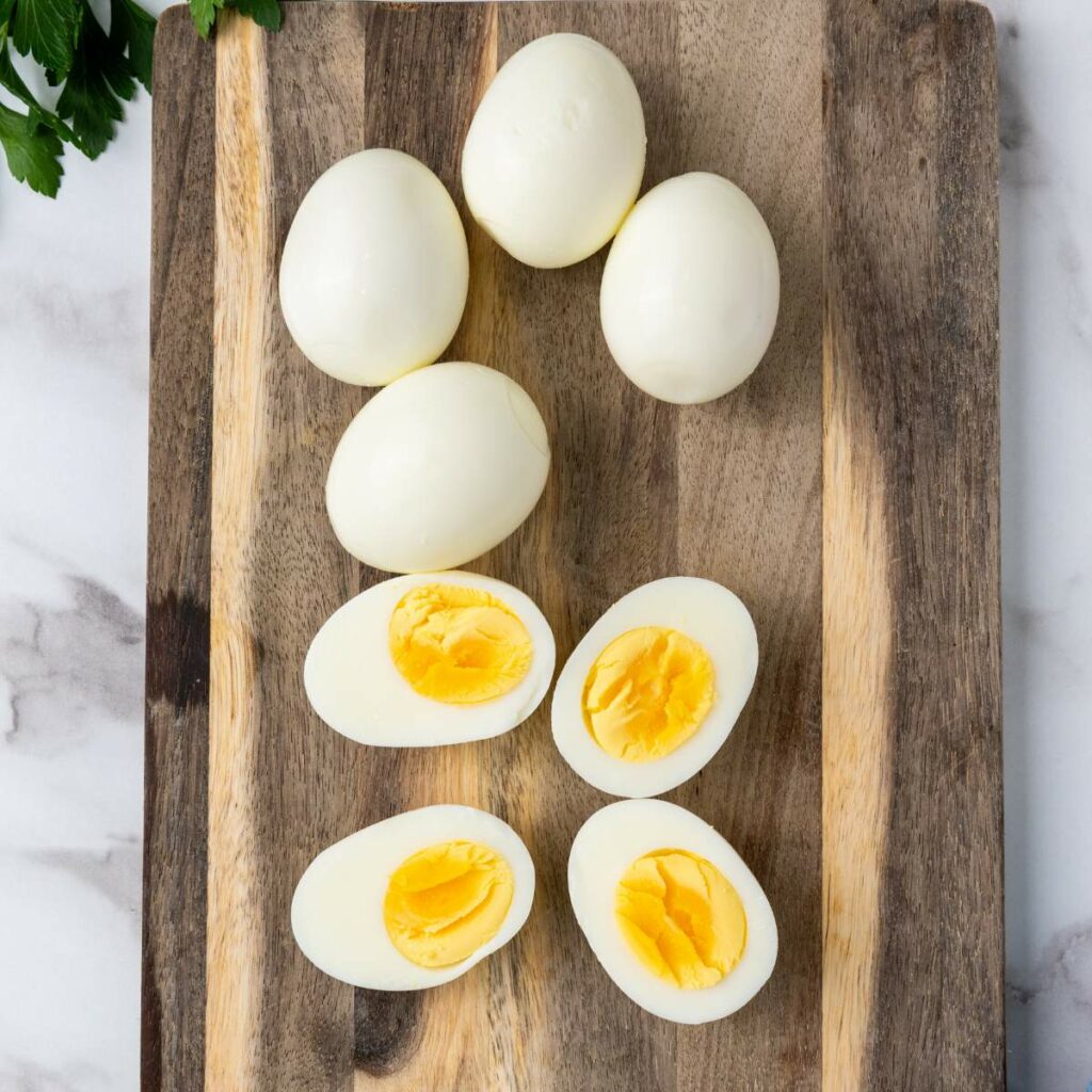 Several hard-boiled eggs, including three cut in half, are arranged on a wooden cutting board.