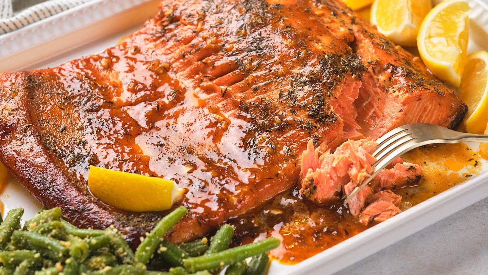 Honey mustard glazed salmon with seasoning, garnished with lemon wedges, served alongside green beans on a white platter.