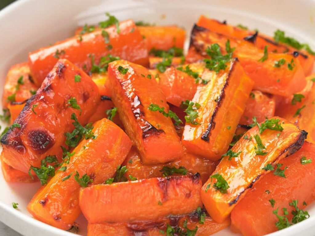 Honey roasted carrots garnished with chopped parsley in a white bowl.
