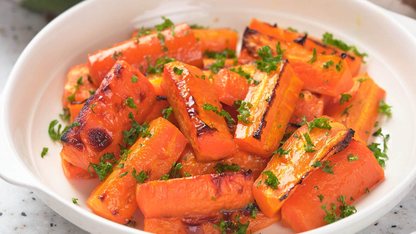 Honey roasted carrots garnished with chopped parsley in a white dish.