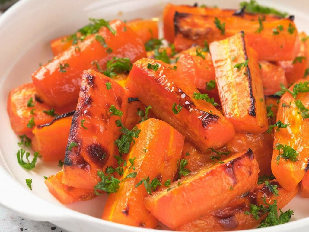 Honey oasted carrot pieces garnished with chopped parsley on a white plate.